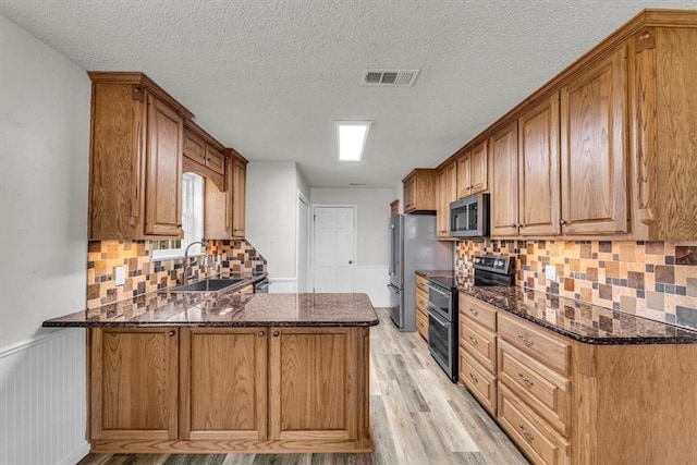 kitchen featuring kitchen peninsula, appliances with stainless steel finishes, sink, light hardwood / wood-style flooring, and dark stone countertops