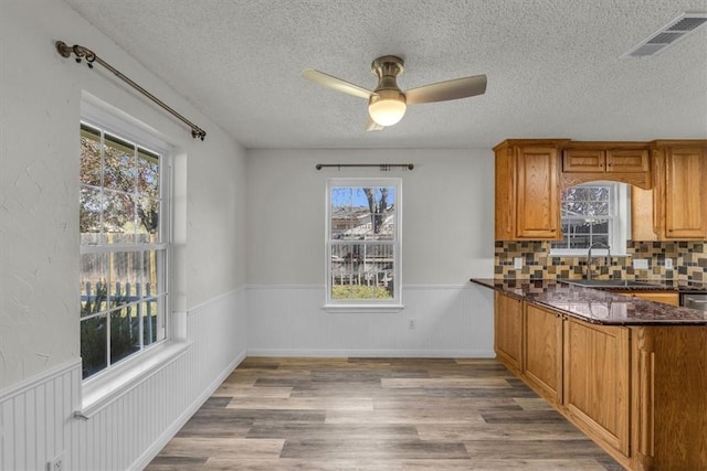 kitchen with sink, backsplash, dark stone counters, and light hardwood / wood-style flooring