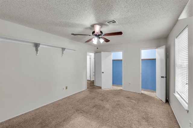 unfurnished bedroom featuring light carpet, a textured ceiling, multiple windows, and ceiling fan