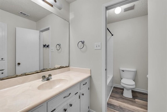 full bathroom featuring washtub / shower combination, wood-type flooring, a textured ceiling, toilet, and vanity