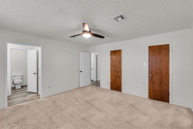 unfurnished bedroom with ensuite bath, light carpet, ceiling fan, and a textured ceiling