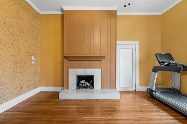 exercise area with a tiled fireplace, ornamental molding, and wood-type flooring