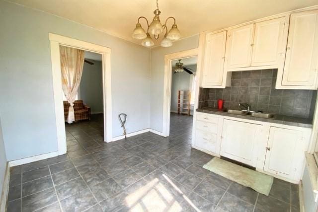 kitchen featuring a sink, baseboards, backsplash, and dark countertops