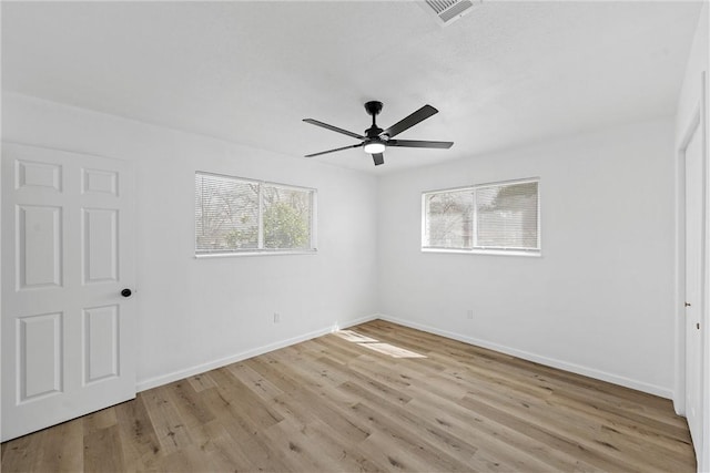 empty room with light wood-style floors, visible vents, baseboards, and a ceiling fan