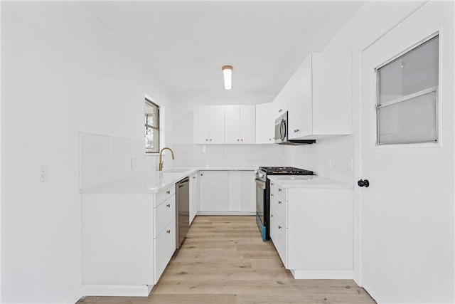 kitchen featuring a sink, stainless steel appliances, light countertops, light wood-type flooring, and backsplash