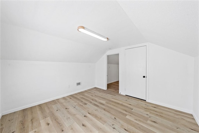 additional living space featuring light wood-style floors, visible vents, baseboards, and vaulted ceiling