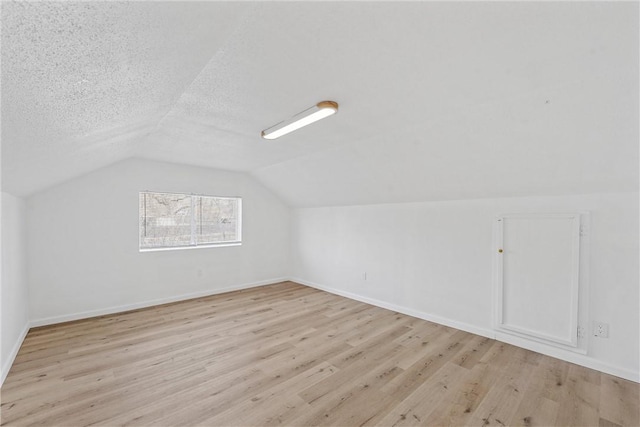 additional living space featuring a textured ceiling, vaulted ceiling, light wood-type flooring, and baseboards