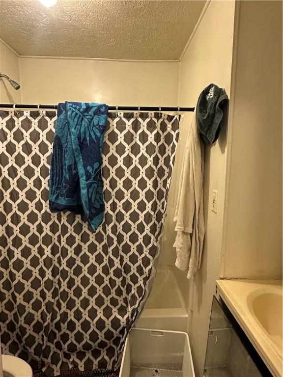 full bathroom with curtained shower, a textured ceiling, and a tub to relax in