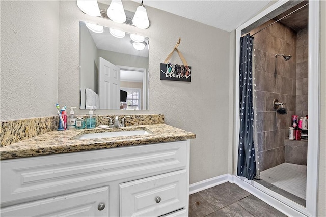 full bath with tiled shower, vanity, and a textured wall