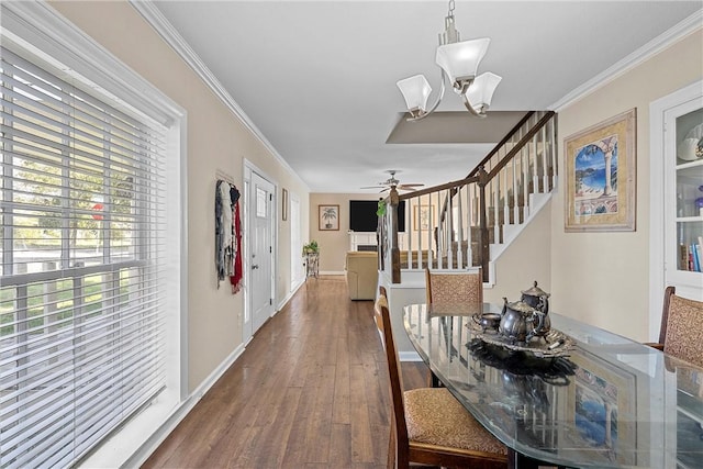 dining room with ceiling fan with notable chandelier, wood-type flooring, crown molding, baseboards, and stairs