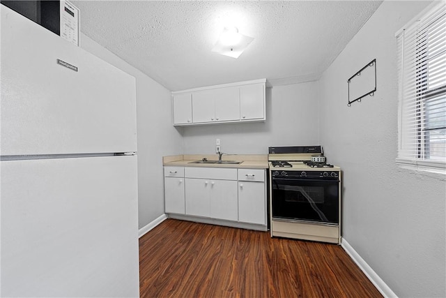 kitchen featuring dark wood-type flooring, light countertops, freestanding refrigerator, gas stove, and a sink