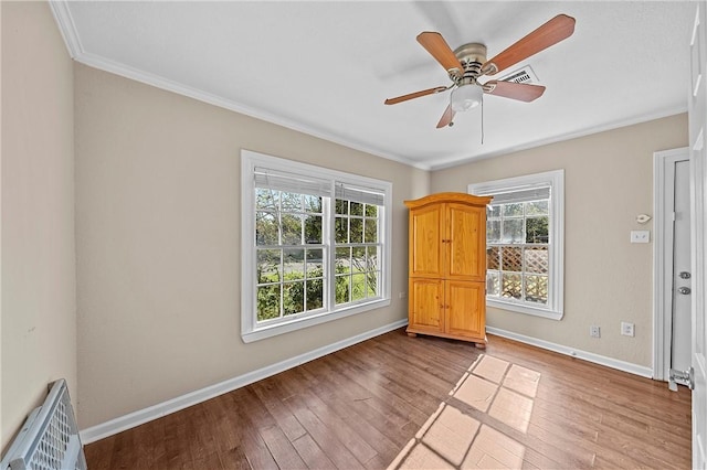 interior space featuring multiple windows, wood-type flooring, baseboards, and ornamental molding