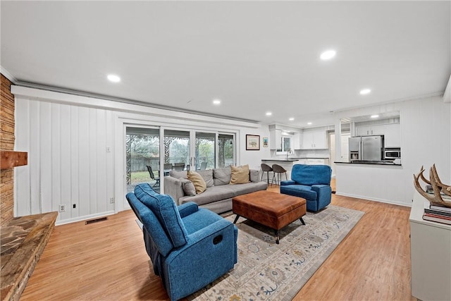 living room featuring a fireplace, light hardwood / wood-style floors, ornamental molding, and sink