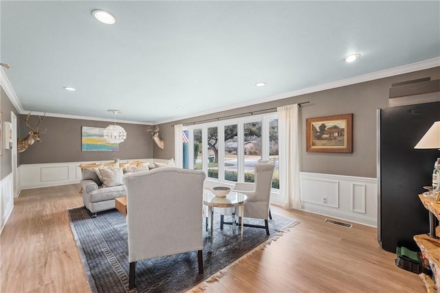 living room with light hardwood / wood-style floors, crown molding, and a notable chandelier