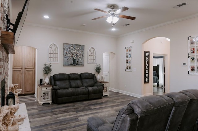 living room with ceiling fan, a stone fireplace, dark hardwood / wood-style flooring, and crown molding