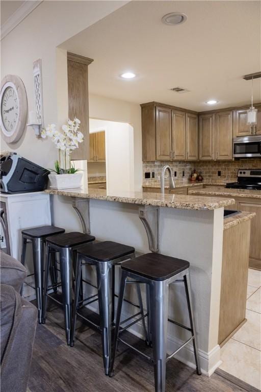 kitchen featuring a breakfast bar, appliances with stainless steel finishes, backsplash, and light stone countertops