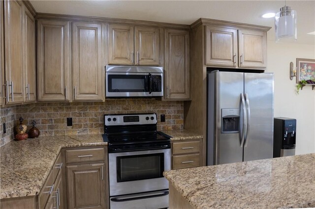 kitchen with light stone countertops, hanging light fixtures, appliances with stainless steel finishes, and tasteful backsplash