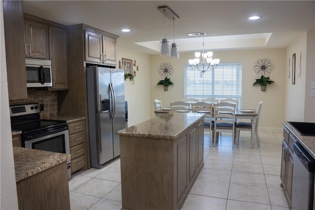 kitchen featuring light stone countertops, backsplash, stainless steel appliances, an inviting chandelier, and a center island