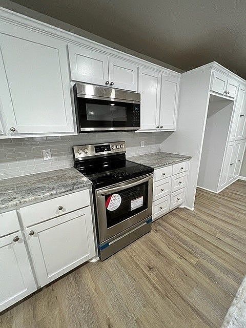 kitchen with white cabinets, light stone counters, appliances with stainless steel finishes, and light hardwood / wood-style flooring