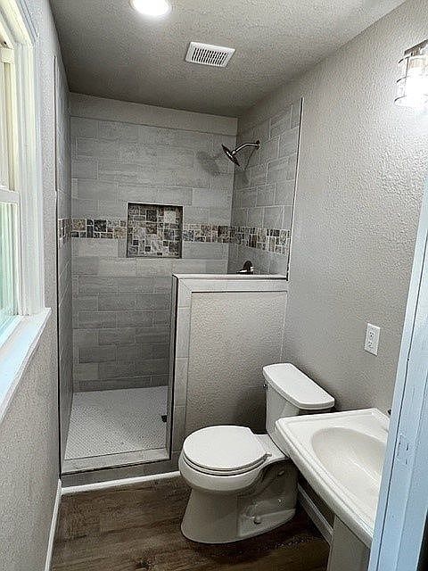 bathroom with toilet, wood-type flooring, sink, and a tile shower