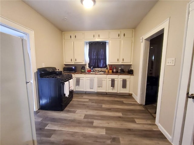 kitchen featuring dark wood-type flooring, sink, white refrigerator, black range with gas stovetop, and white cabinets