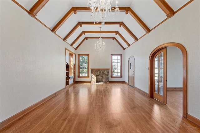 unfurnished living room with an inviting chandelier, hardwood / wood-style floors, beam ceiling, and a fireplace