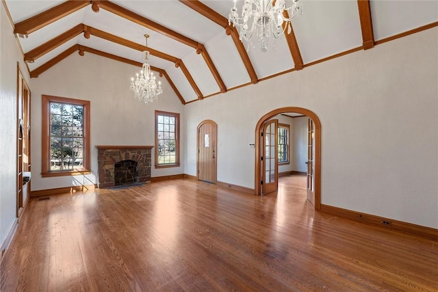 unfurnished living room featuring an inviting chandelier, beam ceiling, high vaulted ceiling, a fireplace, and wood-type flooring