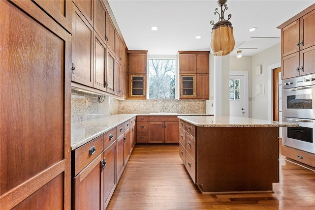 kitchen featuring decorative light fixtures, tasteful backsplash, a center island, stainless steel double oven, and light wood-type flooring