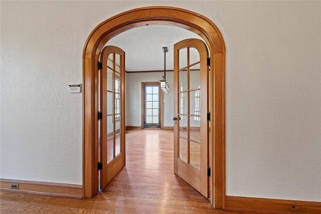 hall with french doors, ornamental molding, and light hardwood / wood-style flooring