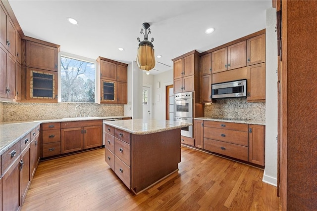 kitchen with decorative light fixtures, a center island, light wood-type flooring, stainless steel appliances, and light stone countertops