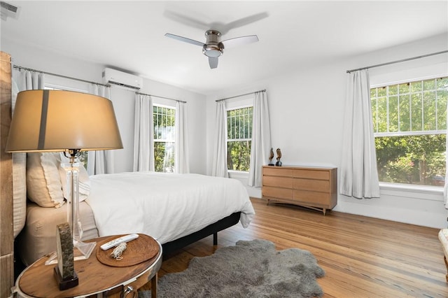 bedroom featuring multiple windows, a wall mounted AC, light hardwood / wood-style floors, and ceiling fan