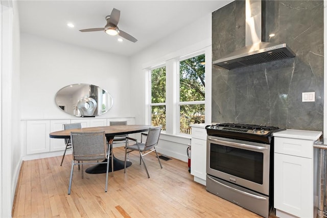 kitchen with white cabinetry, light hardwood / wood-style floors, wall chimney range hood, and stainless steel range with gas stovetop