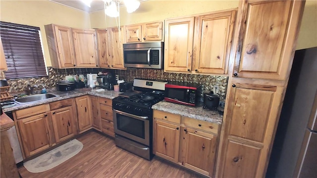 kitchen featuring sink, tasteful backsplash, dark hardwood / wood-style floors, dark stone countertops, and appliances with stainless steel finishes