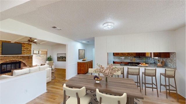 dining space featuring sink, ceiling fan, a fireplace, a textured ceiling, and light wood-type flooring