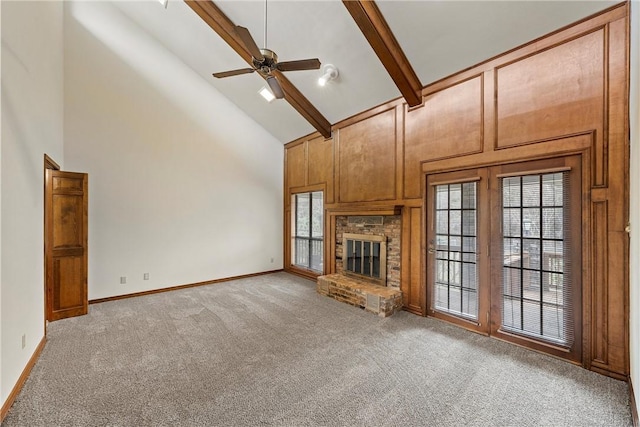 unfurnished living room with beam ceiling, a ceiling fan, a glass covered fireplace, light carpet, and high vaulted ceiling