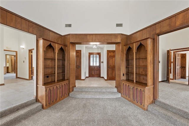 entrance foyer with light carpet, wooden walls, visible vents, and a towering ceiling