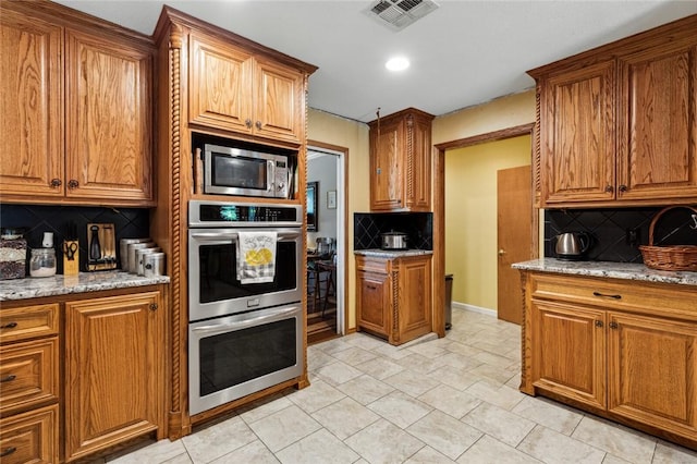 kitchen featuring appliances with stainless steel finishes, tasteful backsplash, and light stone counters