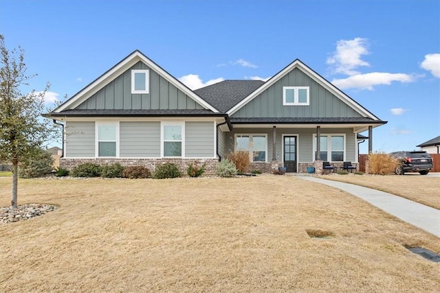 craftsman inspired home featuring a shingled roof, a front lawn, a porch, board and batten siding, and brick siding