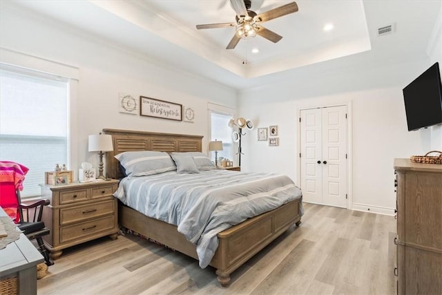 bedroom with baseboards, visible vents, a tray ceiling, light wood-style floors, and recessed lighting