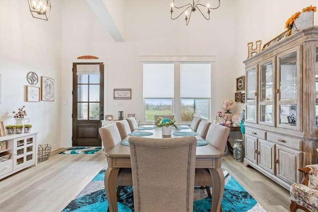 dining space with a chandelier, light wood finished floors, plenty of natural light, and a towering ceiling