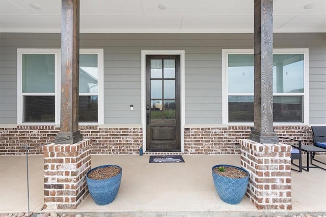 view of exterior entry featuring brick siding and a porch