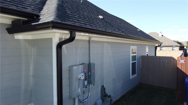 view of side of home featuring a shingled roof and fence