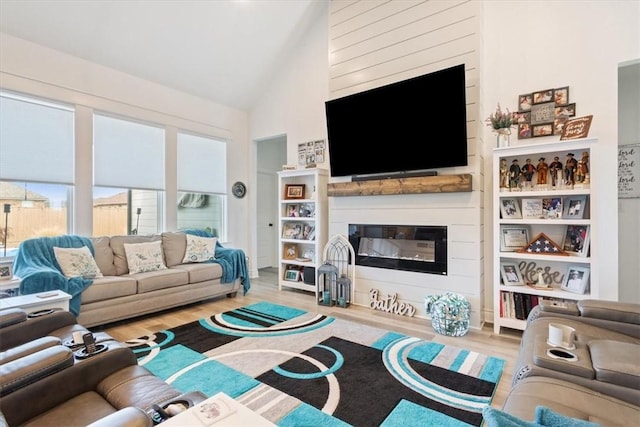 living room with high vaulted ceiling, a glass covered fireplace, and wood finished floors