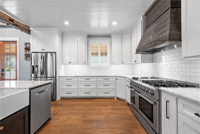 kitchen featuring premium range hood, appliances with stainless steel finishes, wood-type flooring, light stone countertops, and white cabinets