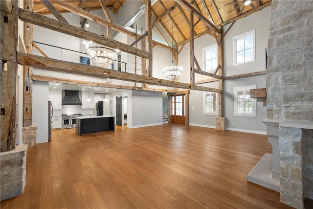 unfurnished living room featuring hardwood / wood-style floors, beam ceiling, high vaulted ceiling, ceiling fan with notable chandelier, and wooden ceiling