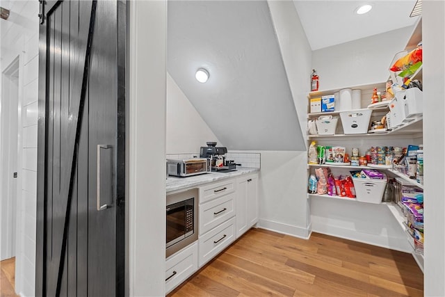 kitchen with light stone countertops, white cabinetry, light hardwood / wood-style floors, a barn door, and built in microwave