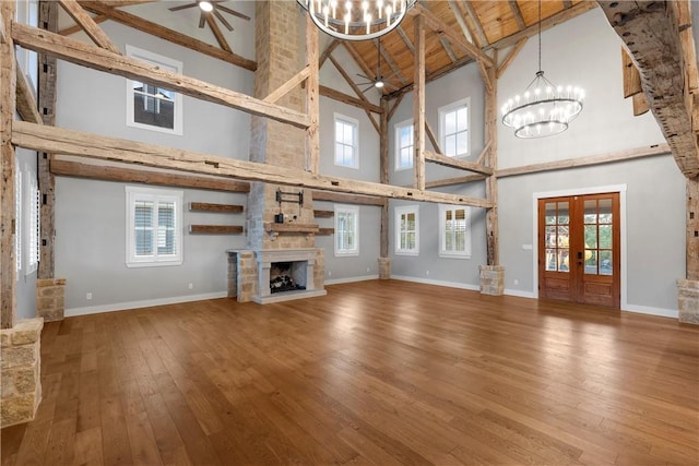 unfurnished living room featuring wood ceiling, plenty of natural light, a stone fireplace, high vaulted ceiling, and french doors