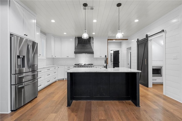 kitchen featuring a barn door, custom exhaust hood, hanging light fixtures, a kitchen island with sink, and stainless steel fridge with ice dispenser