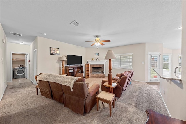 living room featuring a fireplace, washer / dryer, light colored carpet, and ceiling fan