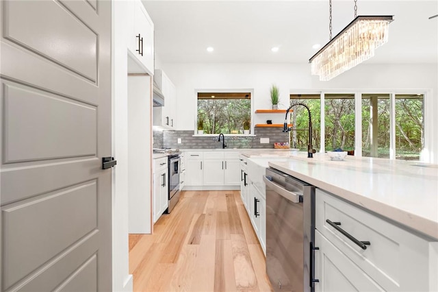 kitchen featuring stainless steel appliances, pendant lighting, light hardwood / wood-style flooring, a notable chandelier, and white cabinets